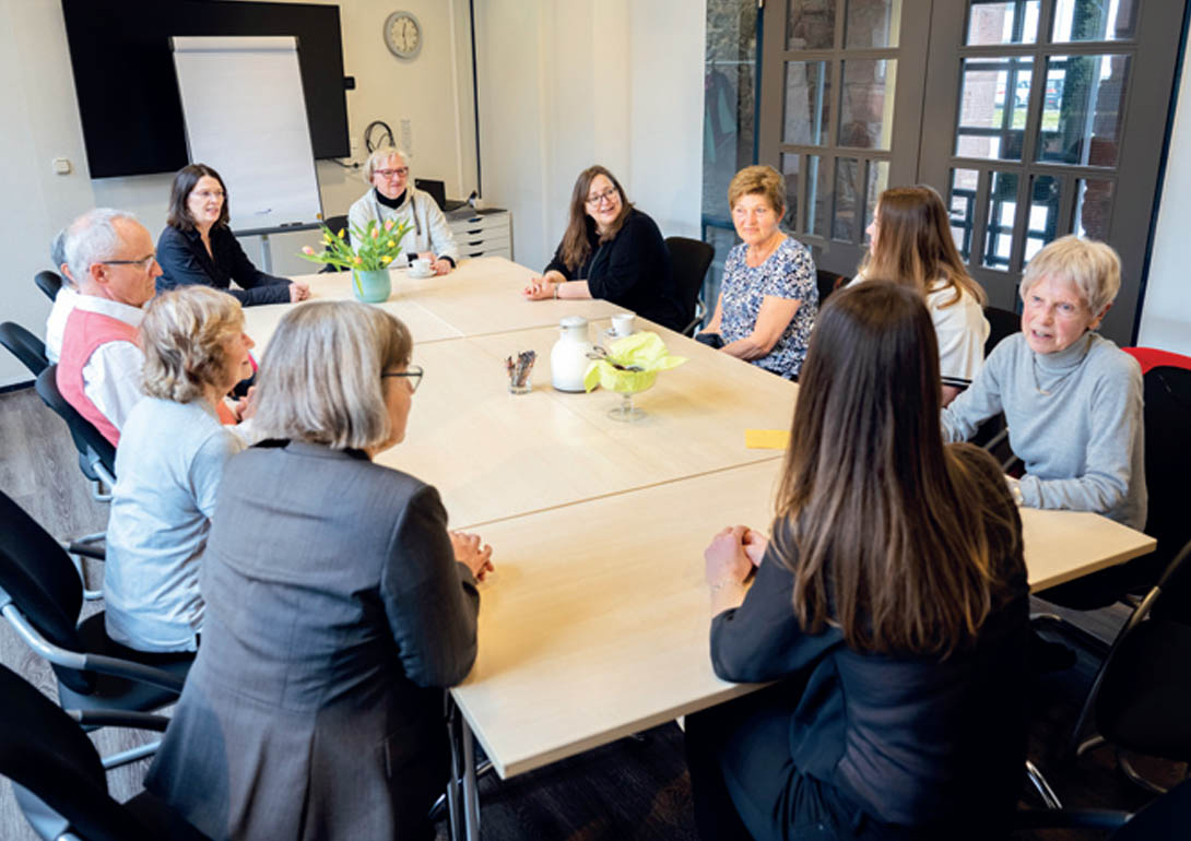 Personen sitzen an einem großen Tisch und sind im Austausch.
